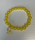 A yellow beaded bracelet with a silver toggle clasp, displayed on a light gray textured surface.