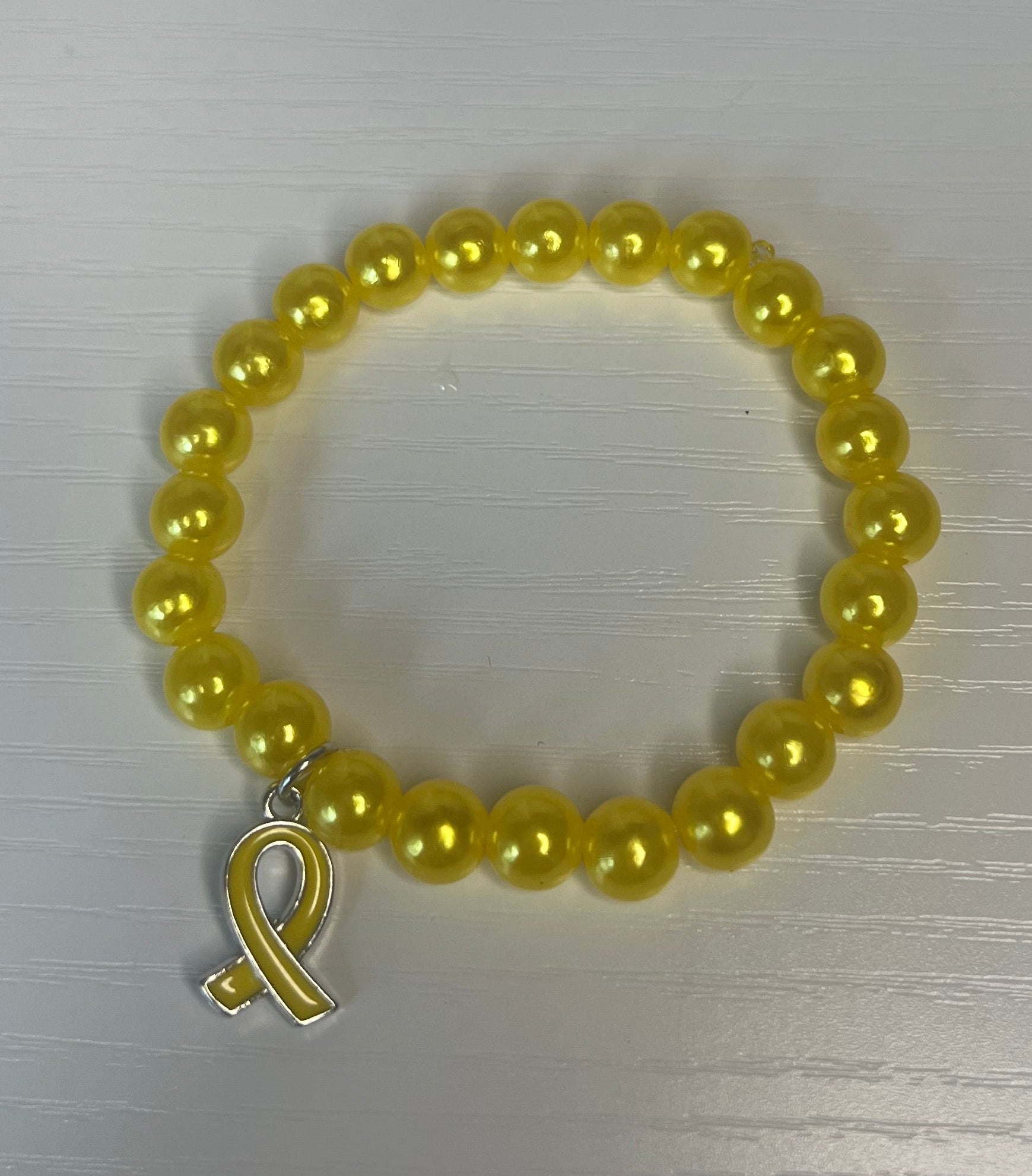 A yellow beaded bracelet with a silver toggle clasp, displayed on a light gray textured surface.